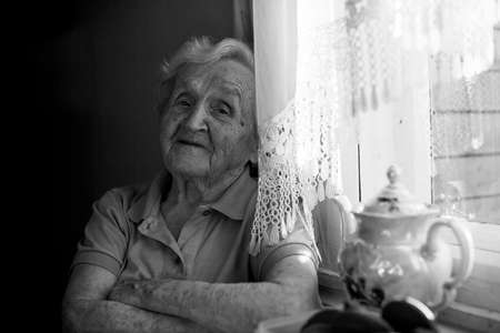An elderly woman sitting at the table with cup of tea. Black and white photo.の写真素材