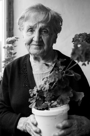 Portrait of old woman standing on the balcony among the flowers. Black-and-white photo.の写真素材