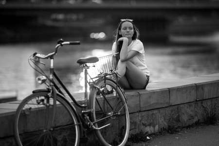 A teen girl with a bicycle sit on the city embankment. Black and white photo.の写真素材