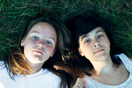 Portrait of two friends girl lying on the green grass in the park.の写真素材