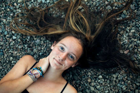 A girl is lying on the sea pebbles. A picture from above.の写真素材
