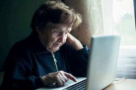 An old woman is typing on a laptop in her home.の写真素材