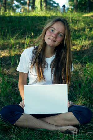 Girl holding clean white sheet paper (banner for message), in the park.の写真素材