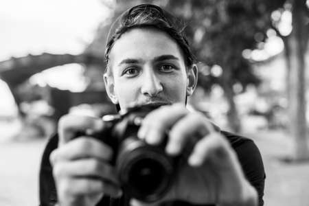 Young handsome emotional man with photocamera outdoors. Black and white photo.の写真素材