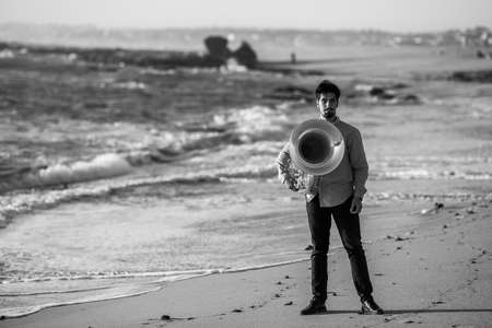 Musician standing with a tuba near the ocean shore. Black and white photo.の写真素材