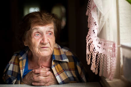 An elderly woman sits thoughtfully at the window.の写真素材