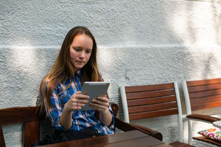 A teengirl sits with a tablet in an outdoor cafe.
