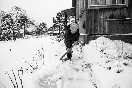 Elderly woman shoveling snow near her rural home. black and white photo.の写真素材