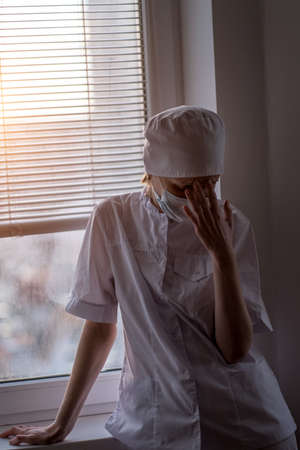 A exhausted female doctor grasping her forehead, wearing a face mask.の写真素材