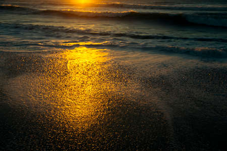 Reflections of the sun on the wet beach sand in beautiful sunset on the Atlantic coast with foamy surf.の写真素材