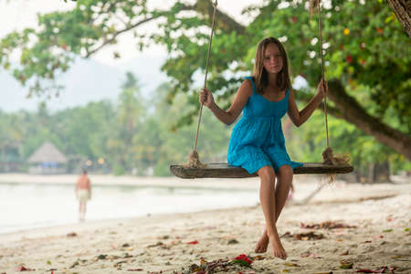 A teenage girl sits on a swing on a tropical beach.の写真素材