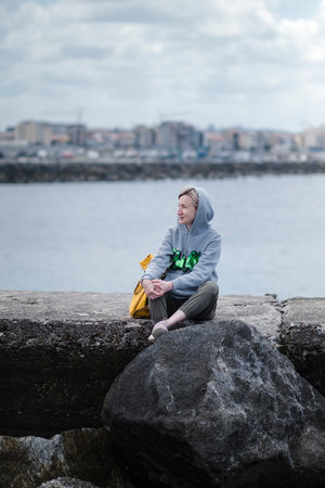 A woman with a backpack sits on the pier at the marina.