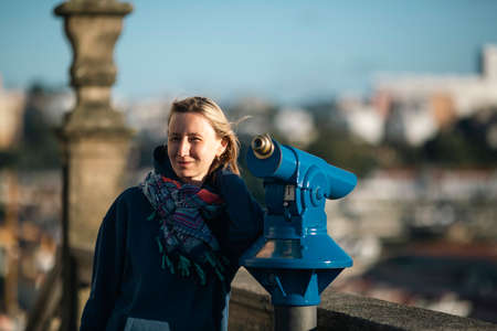 A woman stands by a spyglass at a lookout point in the old town.
