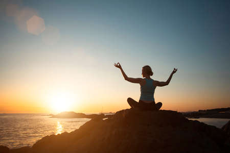 Silhouette of woman practicing yoga on the ocean coast at pleasant sunset.の写真素材