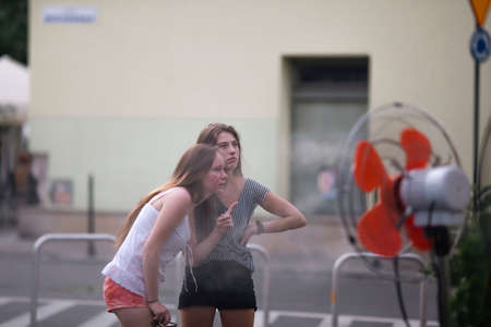 Two girl girlfriends enjoying the fresh air from the fans outside.の写真素材