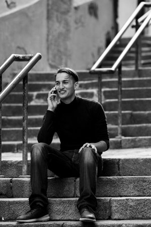 A man sits on the steps of a narrow street and telephone conversation. black and white photo.の写真素材