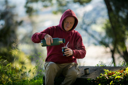 A man in the park pours boiling water from a into a Mate cup.の写真素材
