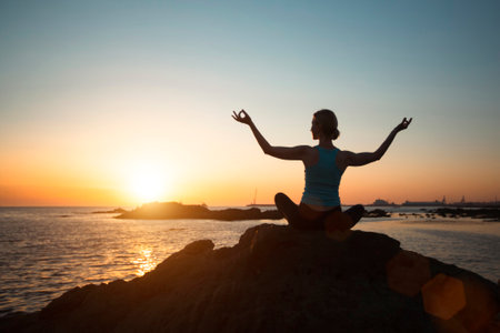 A woman does yoga on a beach at sunset.の写真素材