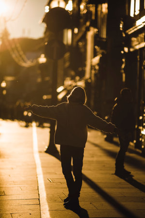 A woman stands on the street in the backlight during a golden sunset.
