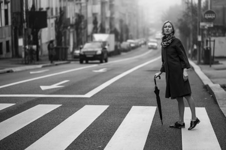 A woman with an umbrella crossing the street in the fog. black and white photograph.の写真素材