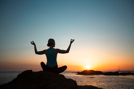 Silhouette of a middle-aged yoga woman on the ocean, during sunset.の写真素材