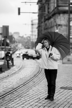 A woman with an umbrella stands on the sidewalk. black and white photo.の写真素材