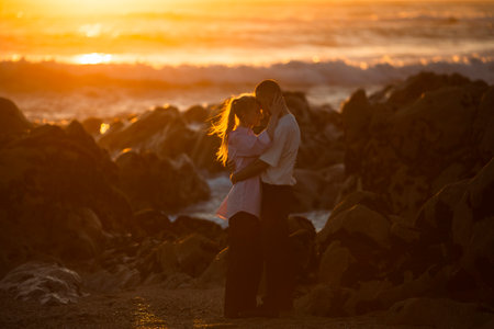 A young couple in love on a romantic date on the rocky coast of the ocean during an amazing sunset.の写真素材