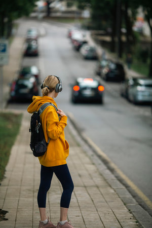 Woman view from behind wearing headphones and carrying a urban backpack on the streets of the city.の写真素材