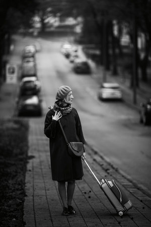 A woman with a suitcase is standing by the side of the road. Black and white photo.の写真素材