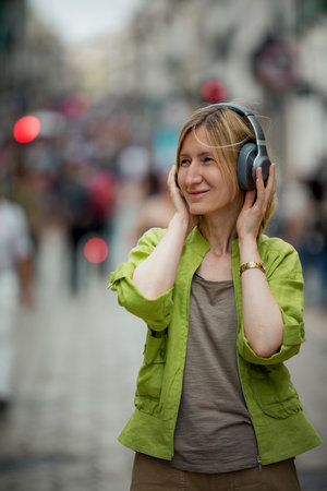 On a crowded street, a woman is listening to music on her headphones.の写真素材