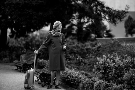 In the square stands a woman with a suitcase in her hands. Black and white picture.の写真素材