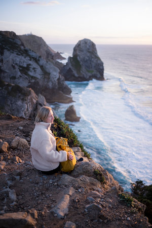 A woman looks out at the ocean sitting on the cliffs, Portugal.の写真素材