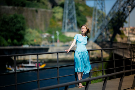 A woman in a blue dress stands on the boardwalk of the riverfront.の写真素材