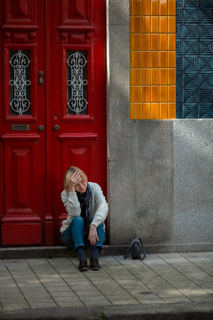 A woman sits on the doorstep of a Portuguese apartment building.の写真素材