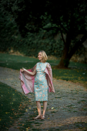 A woman wearing a shawl stands on a path in a park.の写真素材