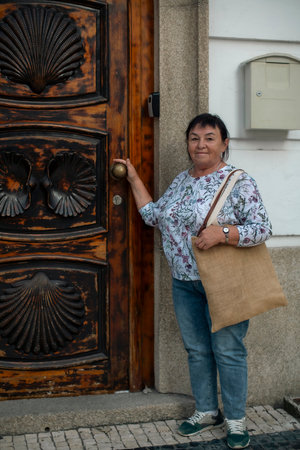Mature female knocking pilgrims on door with shells symbolizing the Way of Santiago.の写真素材