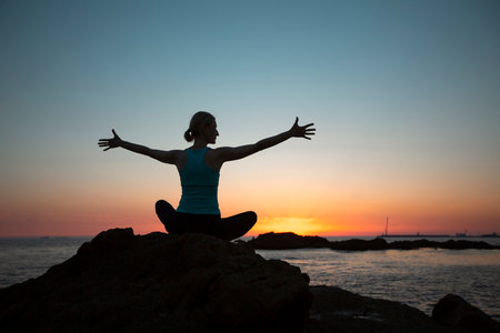 A silhouette of a yoga woman sitting on the seashore at sunset.の写真素材