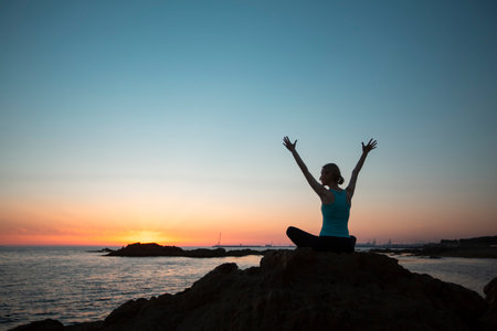 Silhouette of a yoga woman sitting on the seashore at amazing sunset.の写真素材