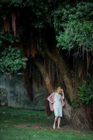 A woman is waiting for a date by a big tree in the park.の写真素材