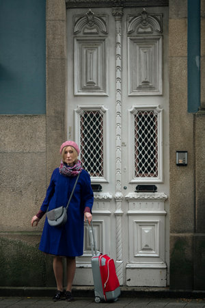 A woman with a suitcase stands at the front door of a building in Portugal.の写真素材