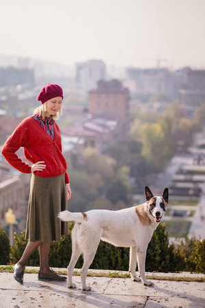 A woman dressed in 70s style stands with a street dog.の写真素材