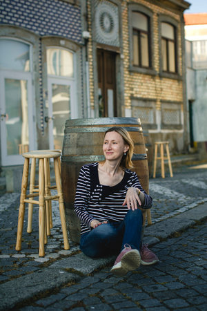 A woman poses sitting on the sidewalk at an outdoor cafe on the waterfront.の写真素材