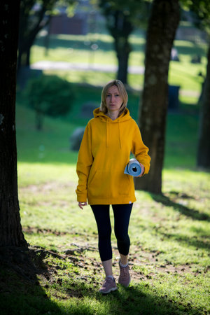 A woman with a yoga mat stands in a city park.の写真素材