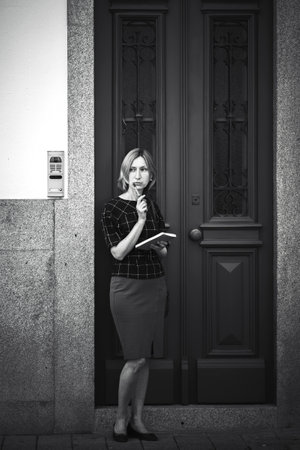 A woman with a notebook stands outside a house. Black and white photo.の写真素材