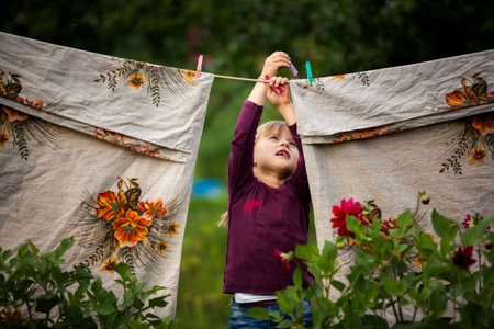 A funny little girl hangs laundry outside a country house.の写真素材