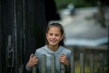 A teenage girl stands by a wooden hedge on a farm.