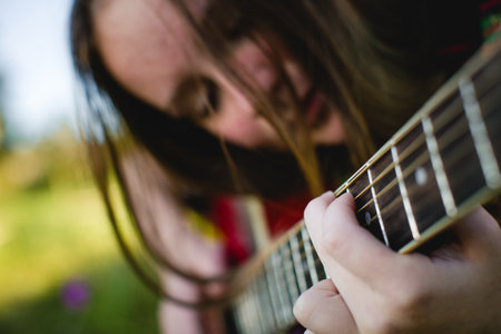 A girl playing the guitar, with the focus on the chords and strings, her face softly blurred in the background.の写真素材