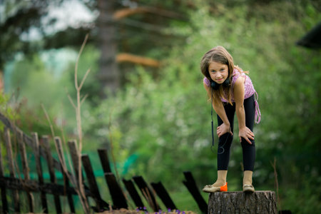 A teenage girl in headphones stands on a tree stump in a village, embracing the tranquility of rural life.の写真素材