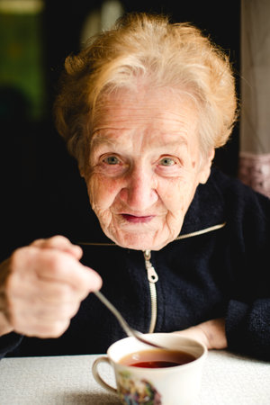 An elderly woman sipping tea, captured in a detailed portrait that highlights her eyes and thoughtful gaze.の写真素材