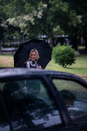 A car approaches and stops near a woman with an umbrella.の写真素材